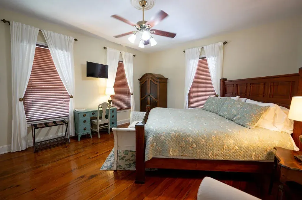 Bright bedroom with a four-poster bed, hardwood floors, striped curtains, and ceiling fan