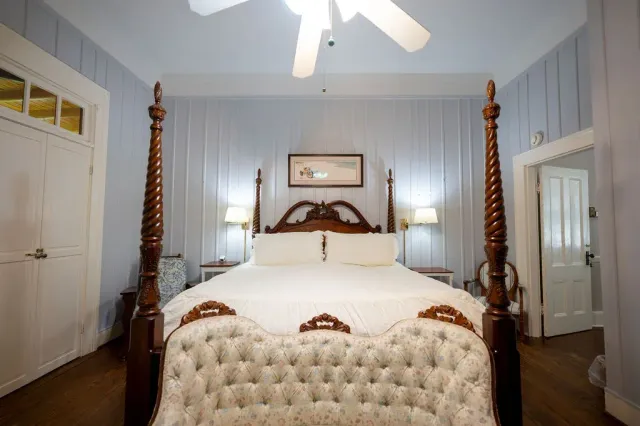 Bright bedroom with a four-poster bed, white bedding, and a ceiling fan under blue walls.