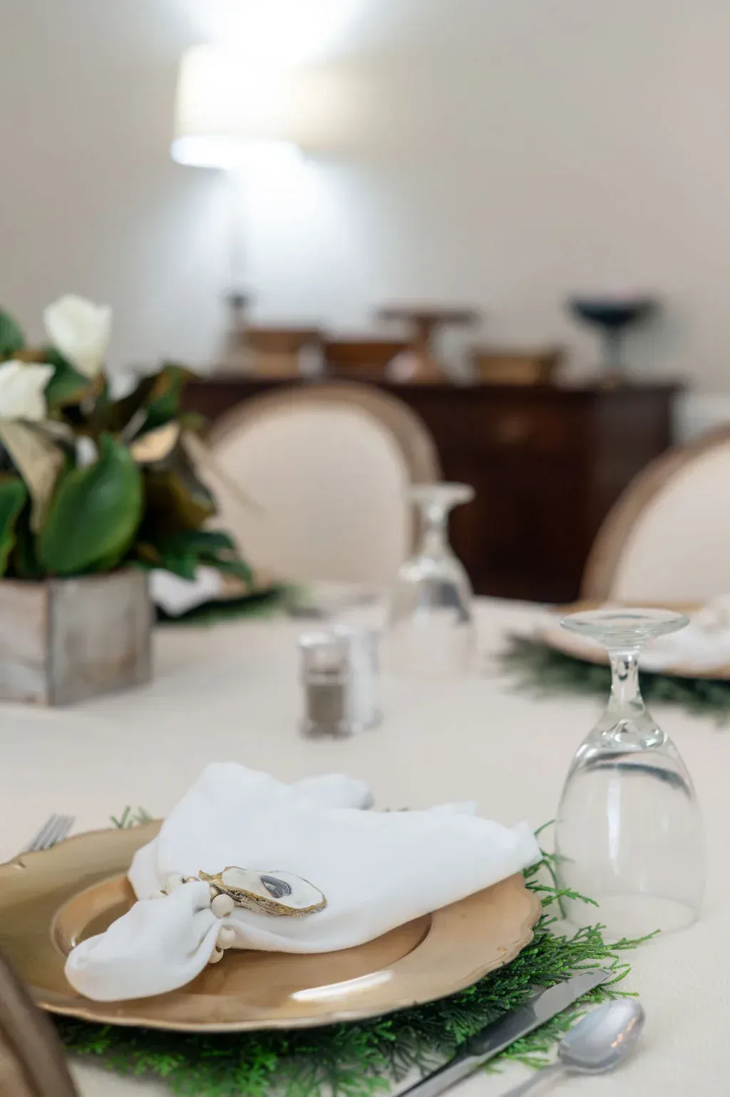 Elegant table setting with white napkin, gold plate, glassware, and greenery in a softly lit room