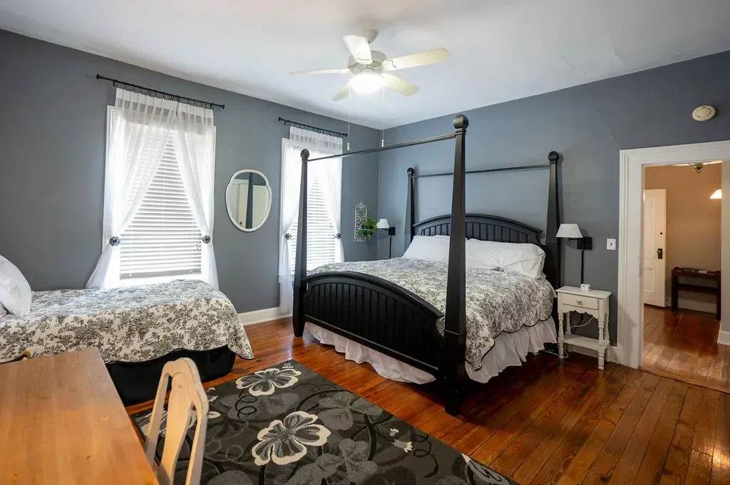 Bright bedroom with two beds, blue walls, wood floors, and a ceiling fan