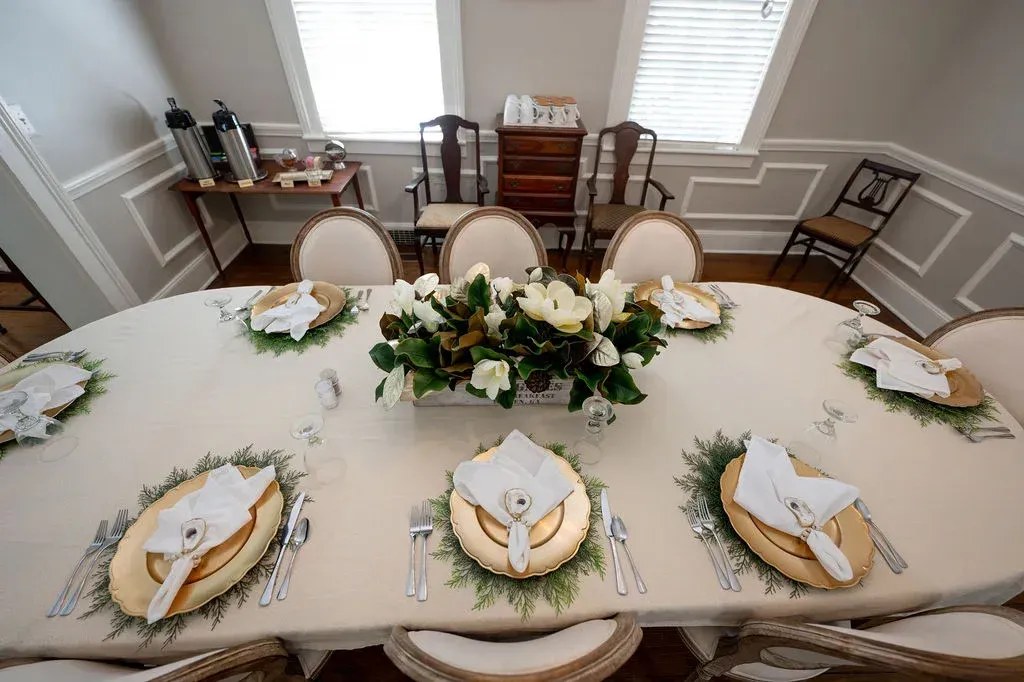 Elegant dining table set with white-and-gold place settings and a floral centerpiece in a bright room