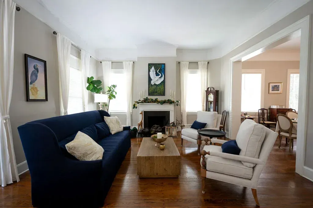 Bright living room with blue sofa, white armchairs, fireplace, and hardwood floors