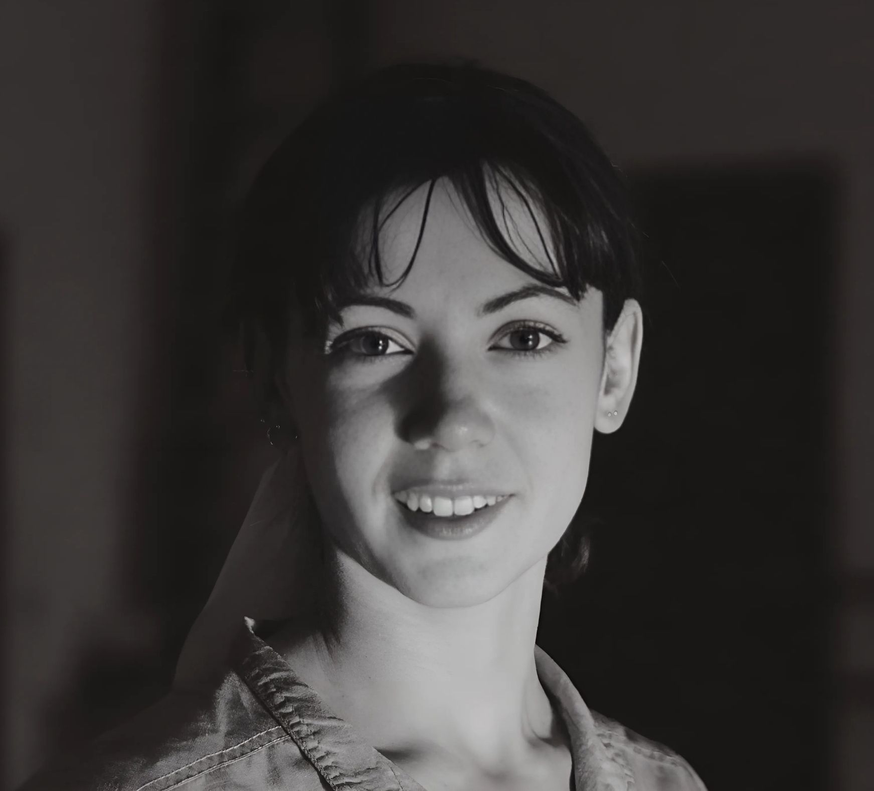 Woman with dark hair, smiling, lit by soft light.
