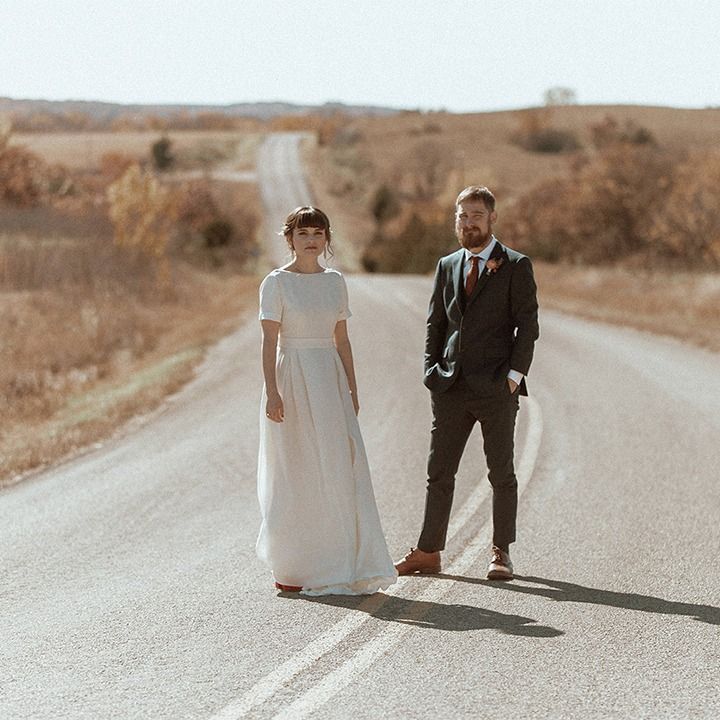 A bride and groom are standing on the side of a road.
