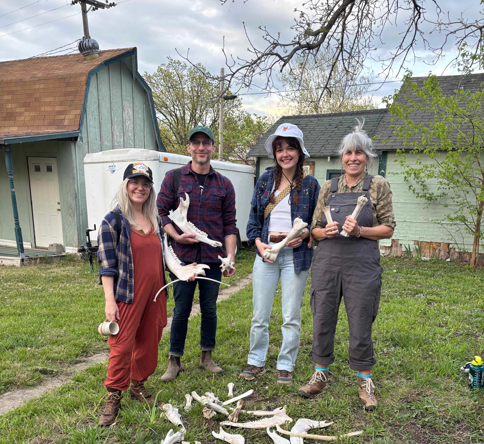 Four people holding animal bones outside. They stand in front of houses with green