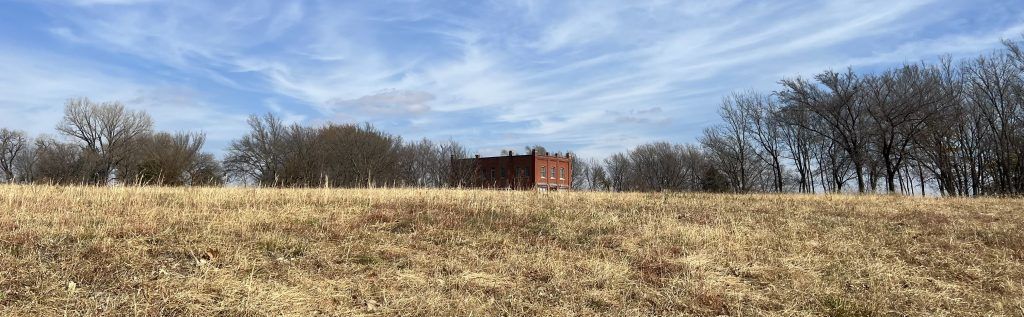 There is a barn in the middle of a field with trees in the background.