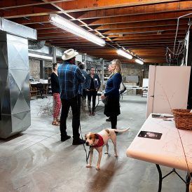 A group of people in a basement setting with a dog, under bright overhead lights.