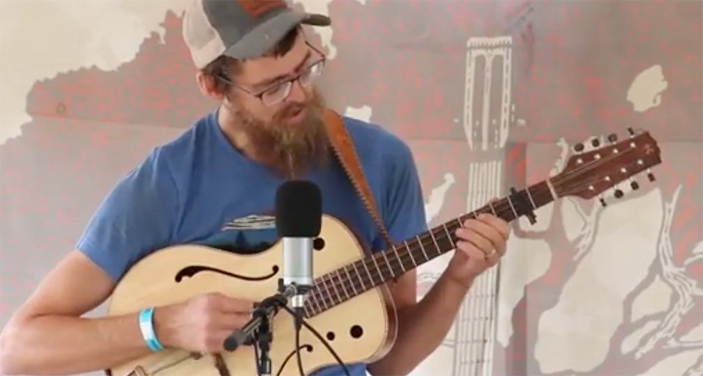 A man with a beard is playing a guitar in front of a microphone.