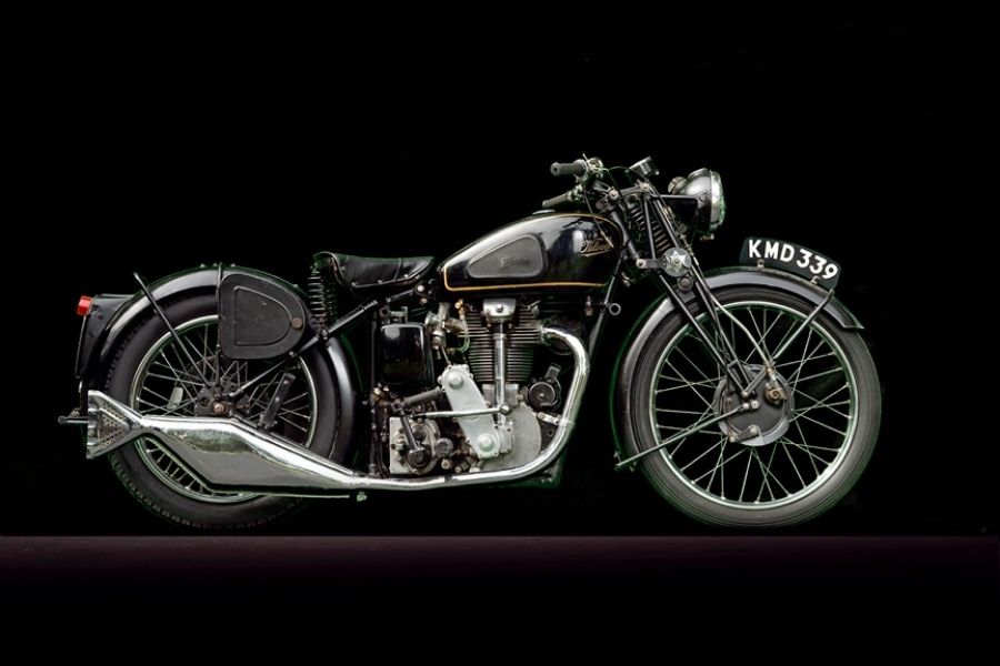 An old black motorcycle is parked on a black background.