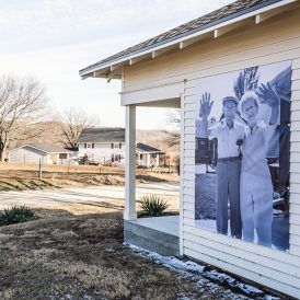 Black and white photo on building of waving couple. A house and road in the background.