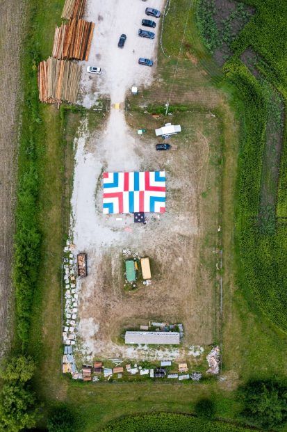 Aerial view: gravel lot with a colorful geometric design and surrounding fields.