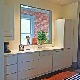 Modern kitchen with white cabinets, a small window showing brick, and a plant.