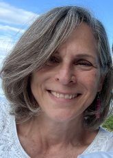 A woman with gray hair is smiling and wearing a white shirt.