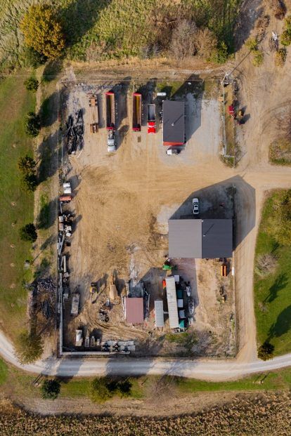 Aerial view of a farm or industrial site with buildings, trucks, and equipment, set in a field.