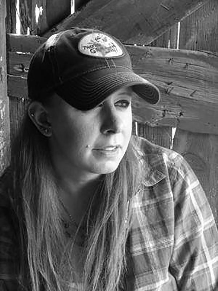 A black and white photo of a woman wearing a hat and plaid shirt.