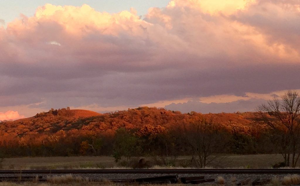 There is a train track in the foreground and a sunset in the background.