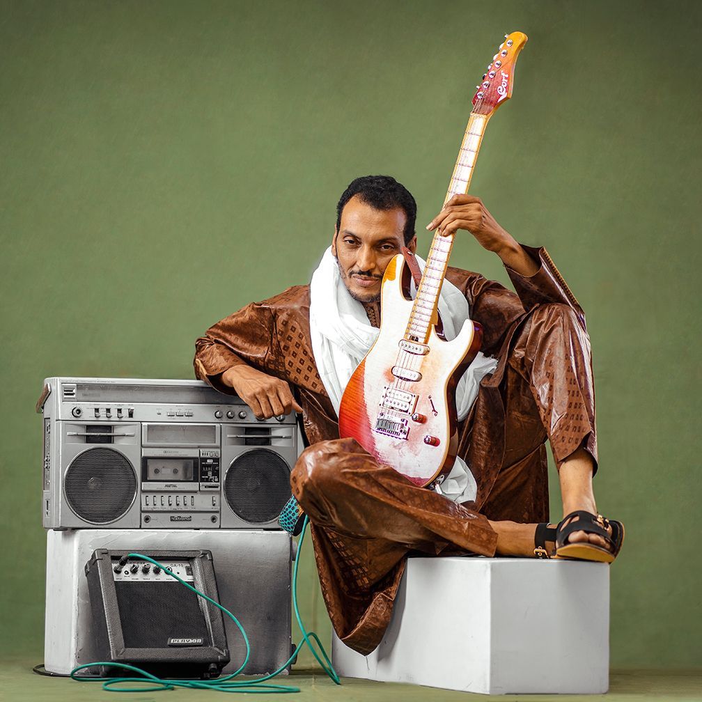 A man is sitting on a box holding a guitar and a boombox
