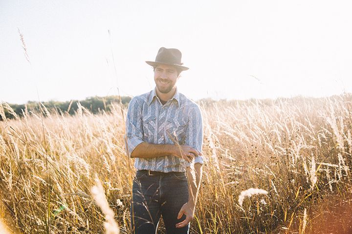 A man in a hat is standing in a field of tall grass.