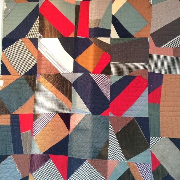 Patchwork quilt, geometric design in various colors: red, blue, brown, beige, and patterned fabrics.