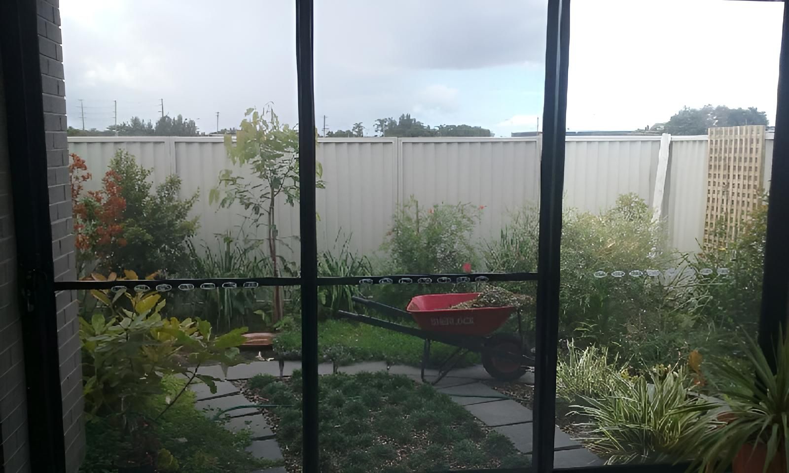 A Red Wheelbarrow Is Parked in The Backyard of A House — Grainger Windows & Doors in Wardell, NSW