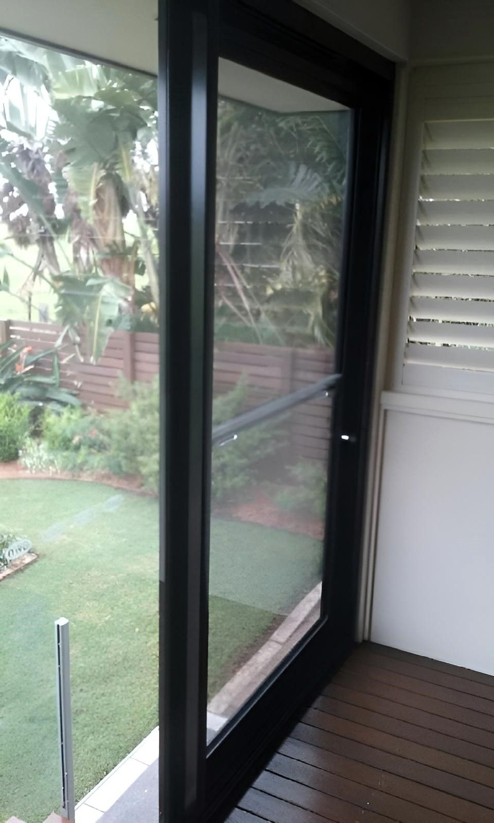 A Sliding Glass Door Leading to A Deck with A View of A Garden — Grainger Windows & Doors in Wollongbar, NSW