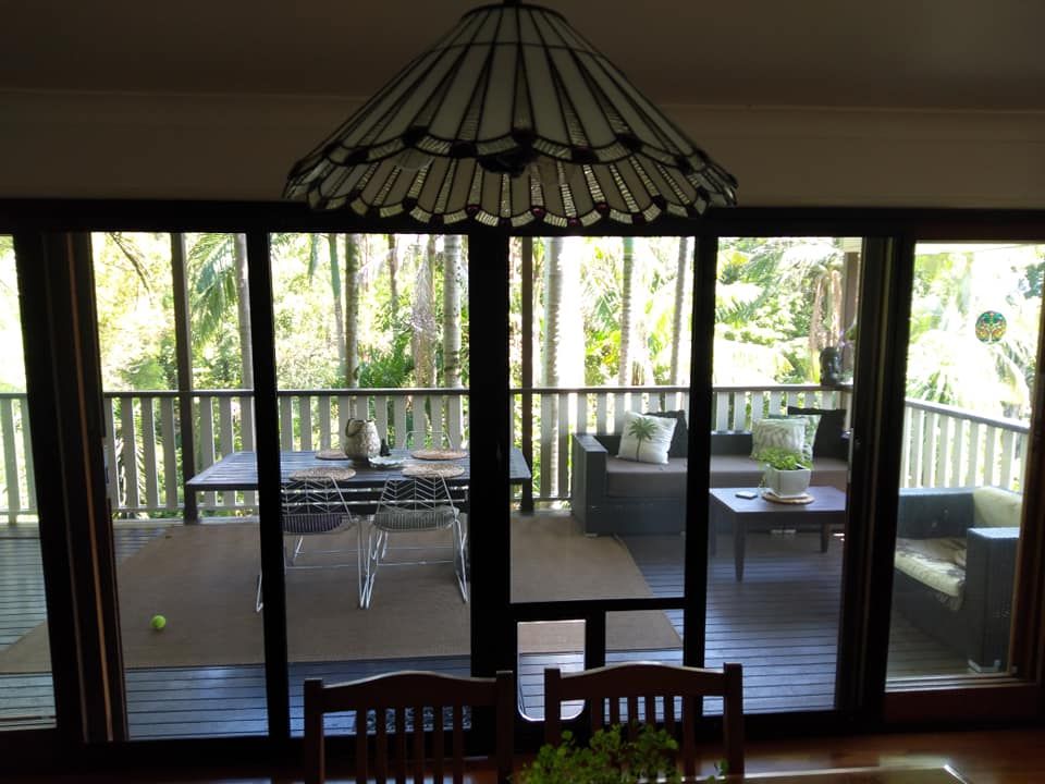 Deck viewed through sliding glass doors, with chairs, table, and striped canopy under a hanging lamp.