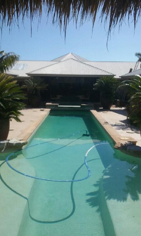 A Large Swimming Pool in Front of A House with A Thatched Roof — Grainger Windows & Doors in Ballina, NSW