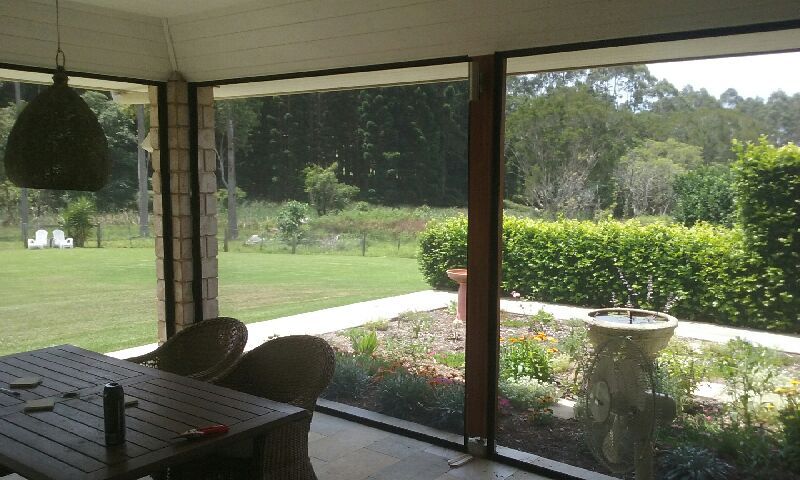 A Screened in Porch with A Table and Chairs and A View of A Garden — Grainger Windows & Doors in Ballina, NSW