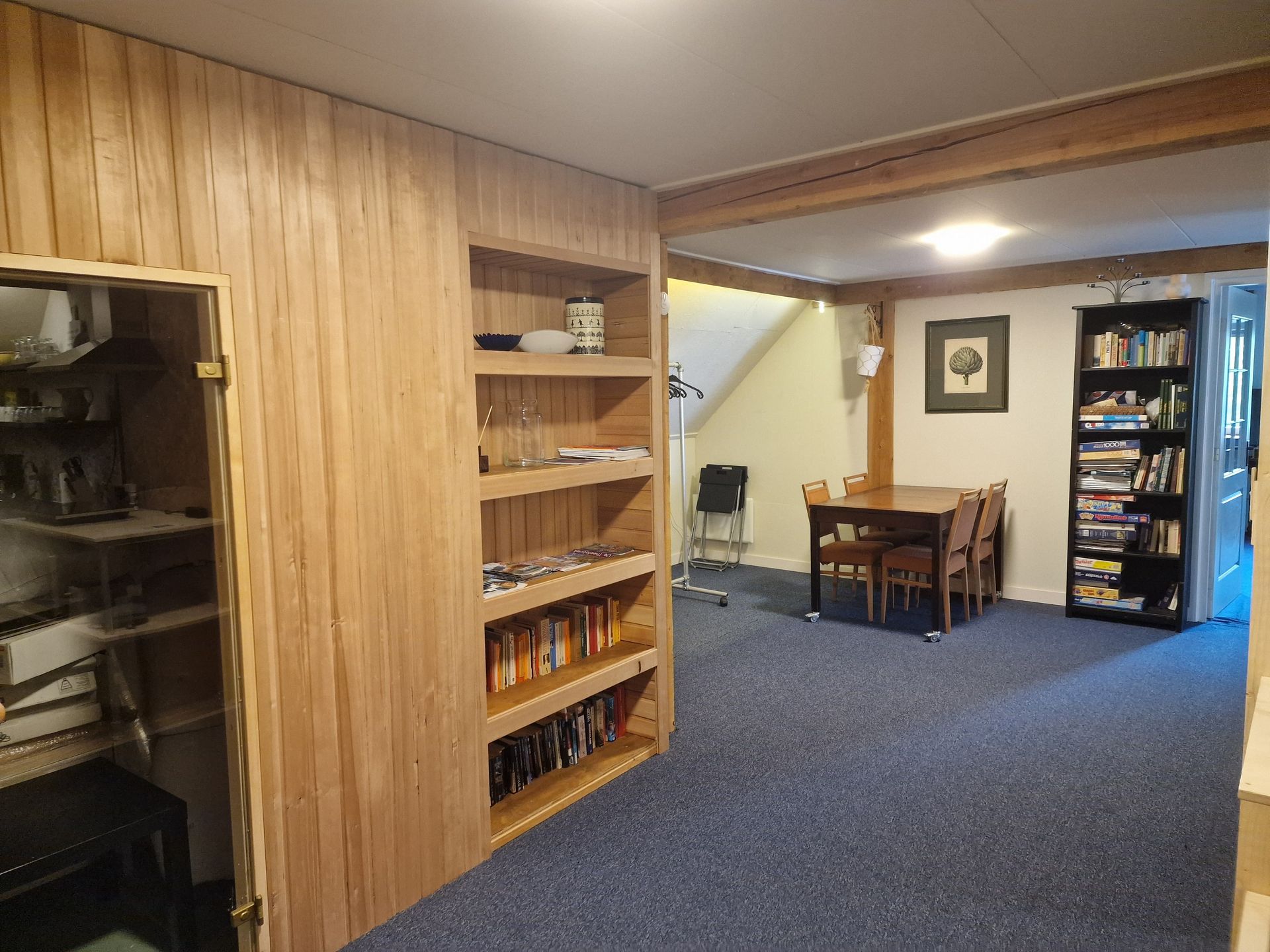 Recreatieruimte in de kelder met houten lambrisering, vloerbedekking, planken, een bureau en een automaat.