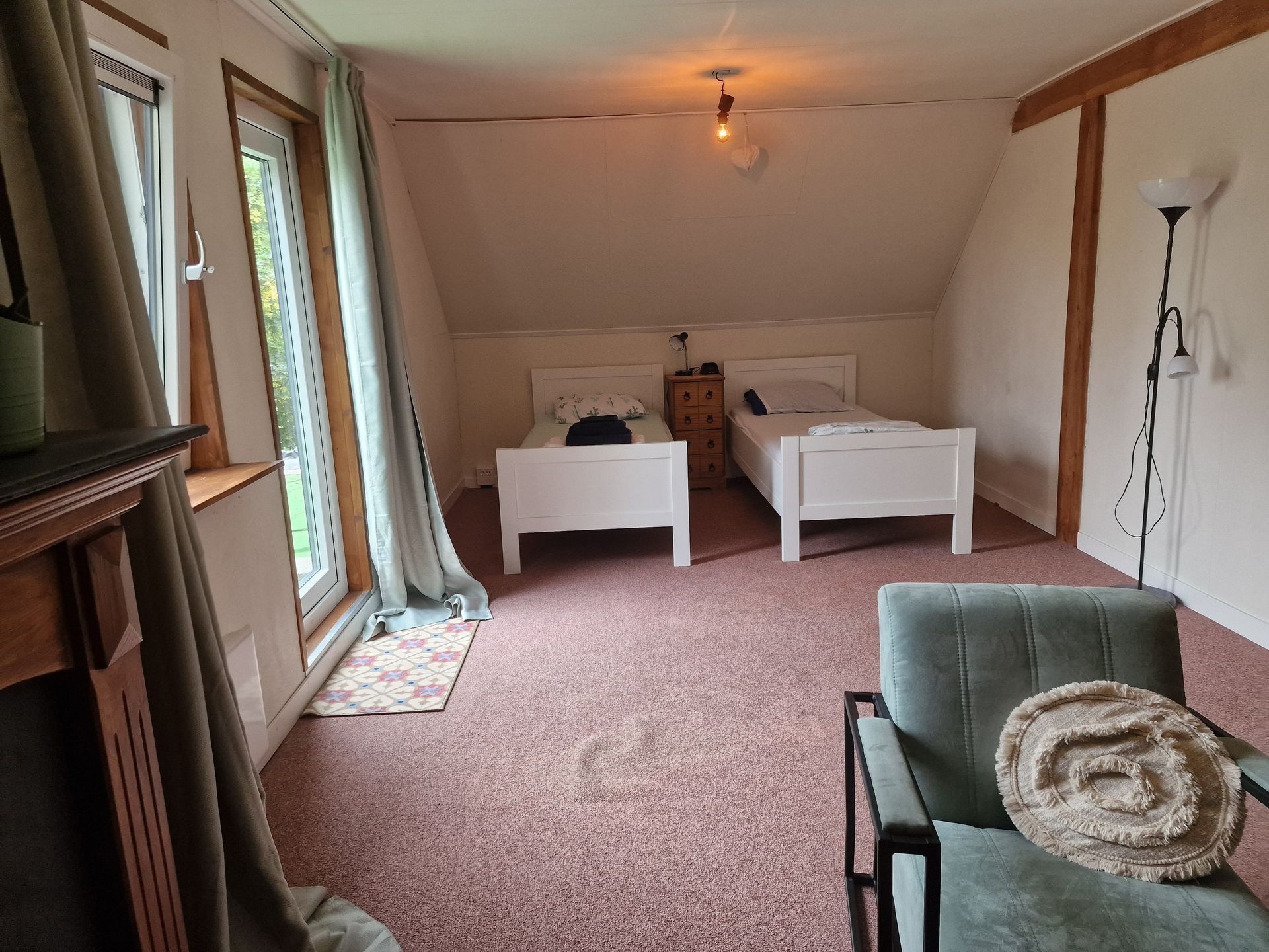 Gezellige zolderkamer met twee witte bedden, roze vloerbedekking, ramen en een groene bank op de voorgrond.