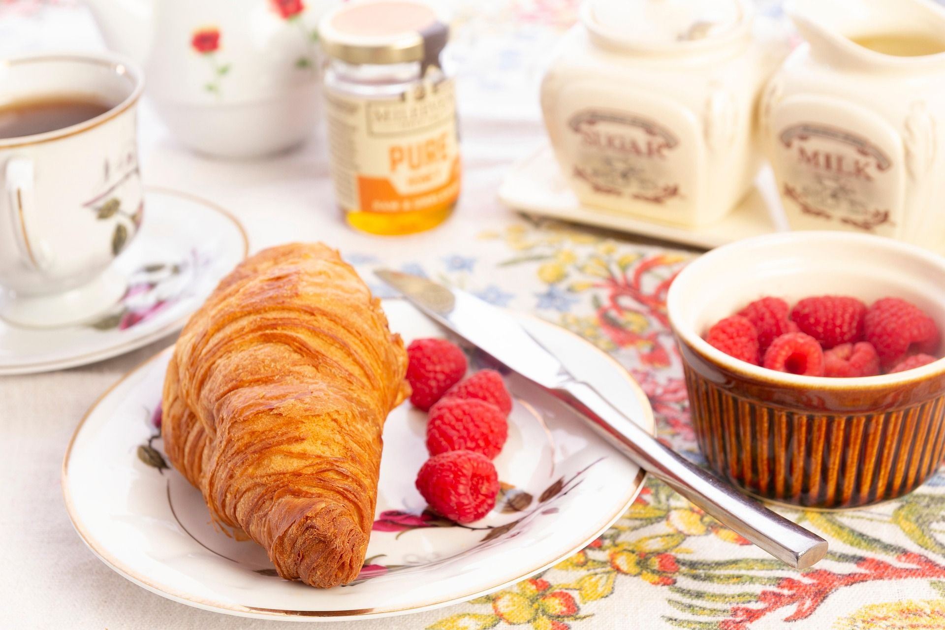 Een croissant op een bord met frambozen, een mes en een schaal aardbeien op een bloementafelkleed.