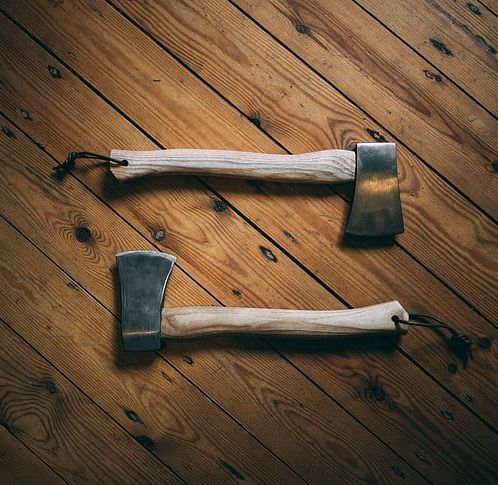 Two axes are sitting on a wooden floor.