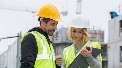 A man and a woman are looking at a clipboard on a construction site.