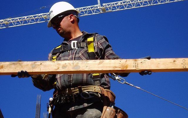 A construction worker is holding a piece of wood in front of a crane.
