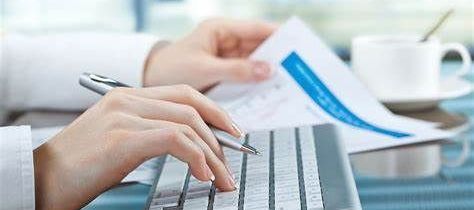 A person is typing on a computer keyboard while holding a pen.