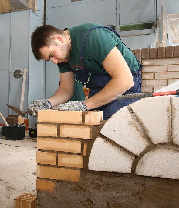 A man in a green shirt is working on a brick wall