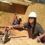 A woman wearing a hard hat is using a circular saw on a construction site.