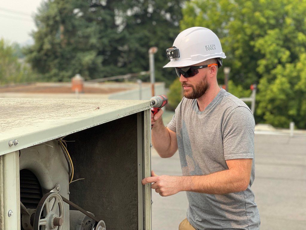 A man wearing a hard hat and sunglasses is working on an air conditioner.