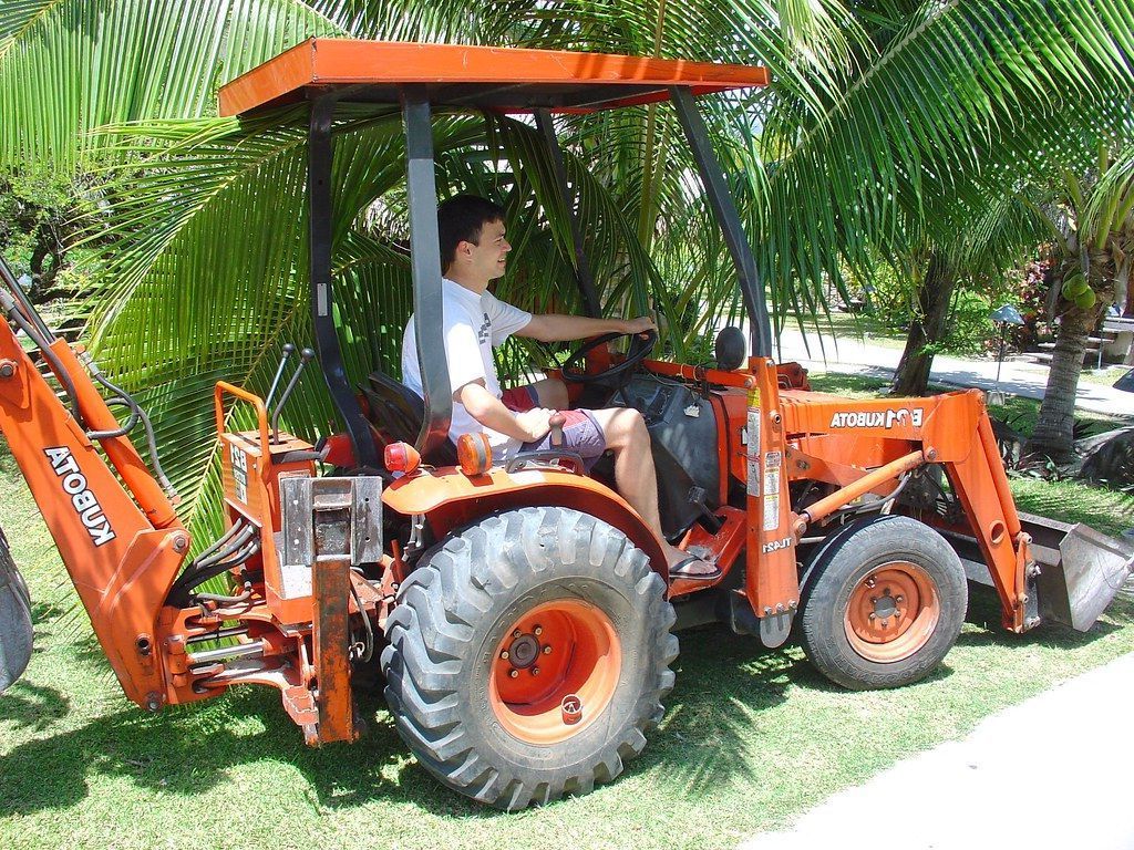 A man is driving an orange tractor with a backhoe attached to it.