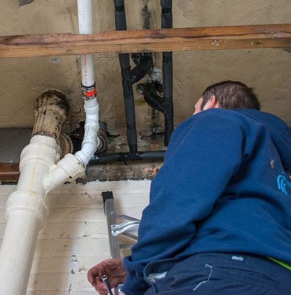 A man in a blue sweatshirt is working on a pipe