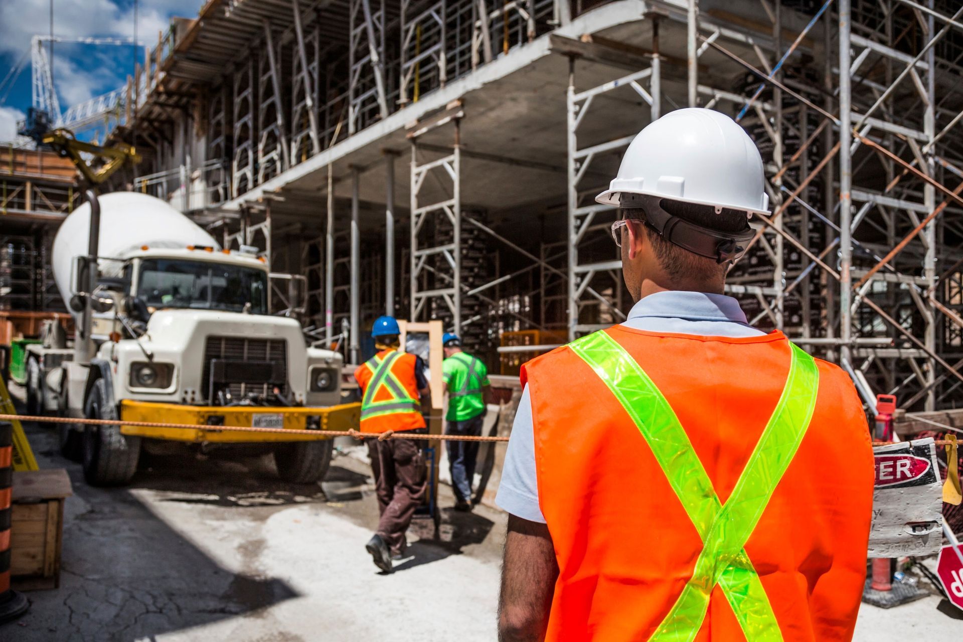 A man in an orange vest and hard hat is standing in front of a construction site.