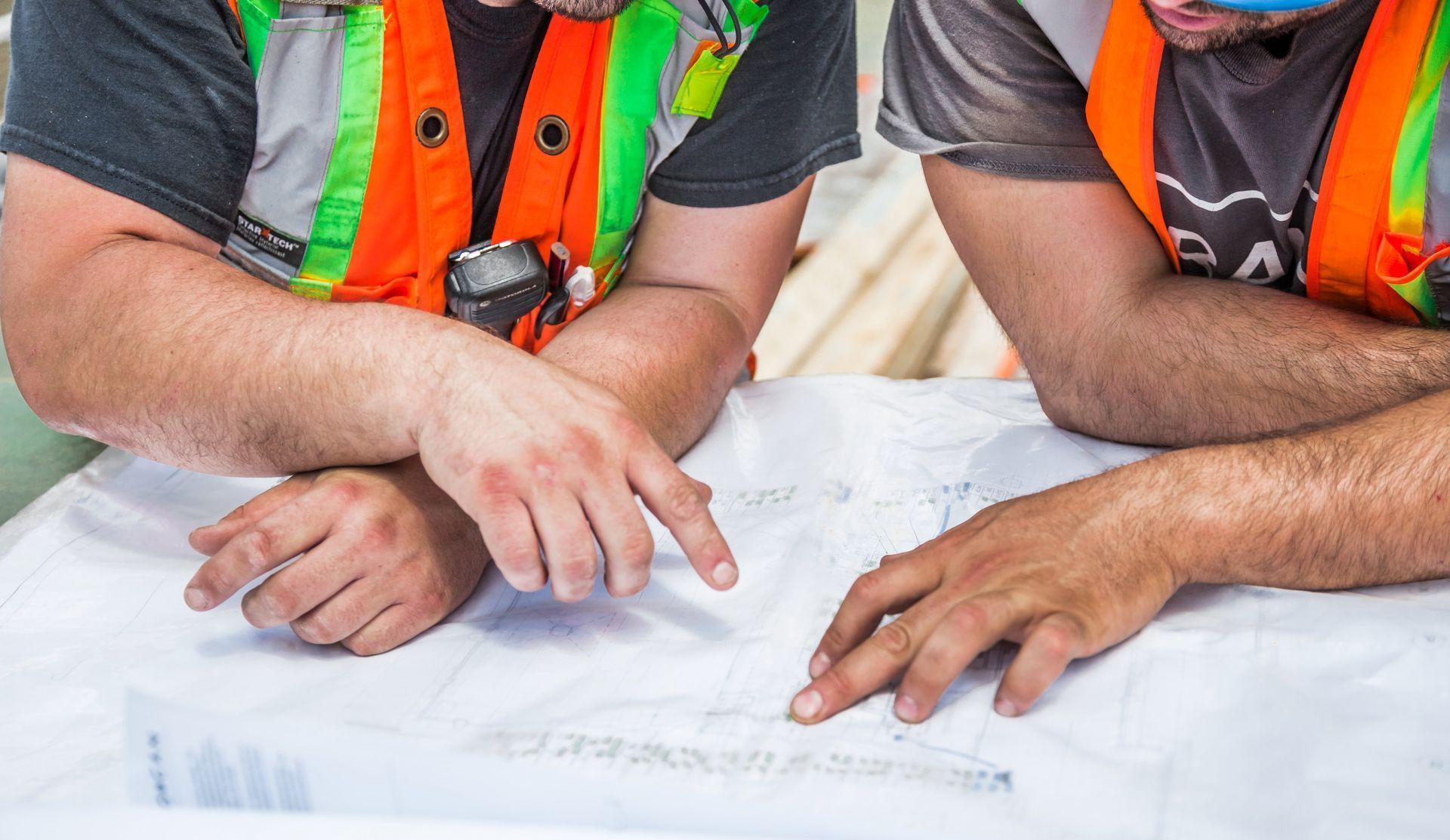 Two construction workers are looking at a blueprint on a table.