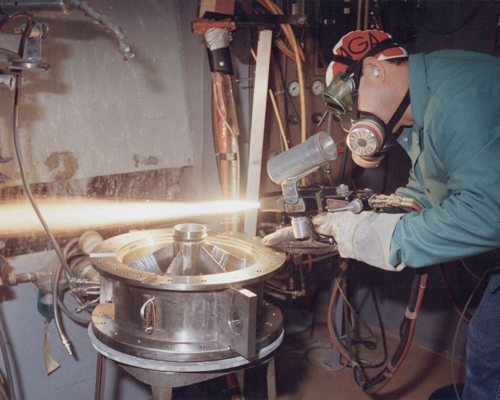 A man wearing a gas mask is working on a piece of metal.