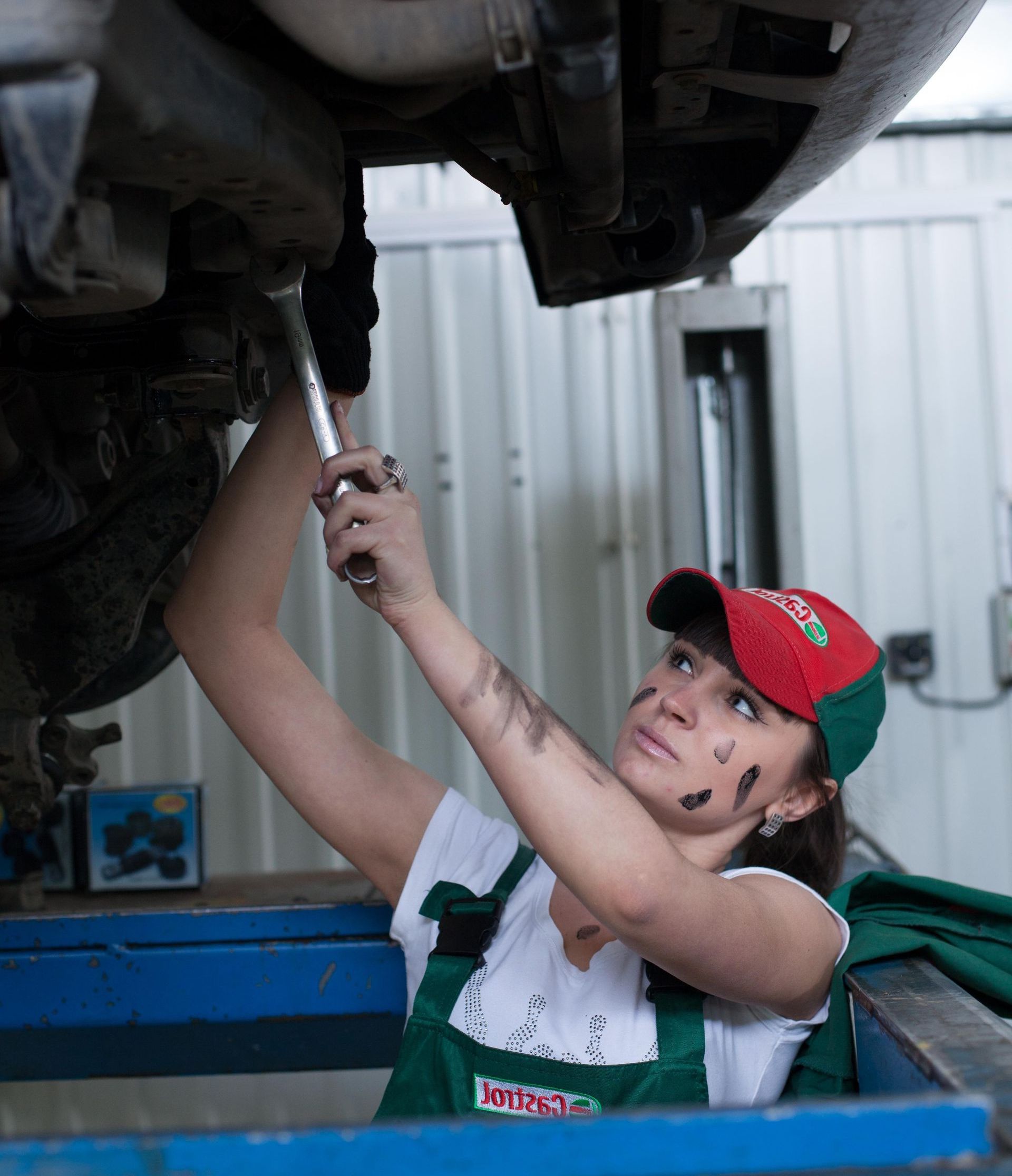 A woman is working under a car with a wrench.