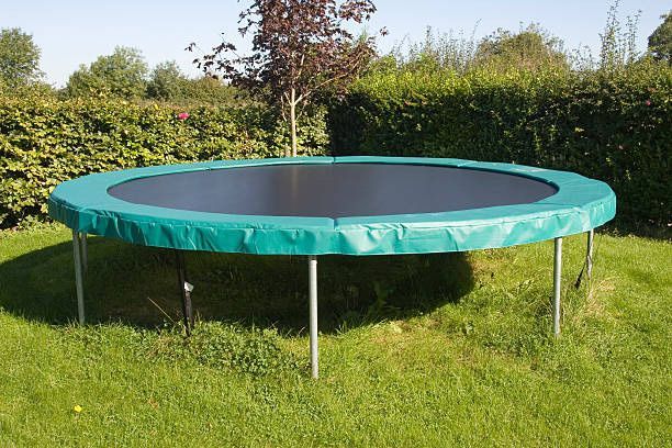 Round green trampoline in a grassy backyard.