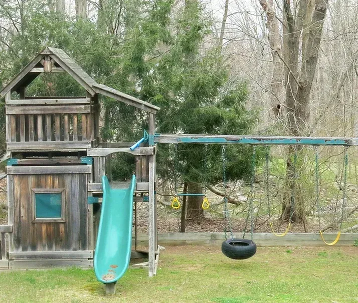 Wooden backyard playset with a house structure, slide, and swings.