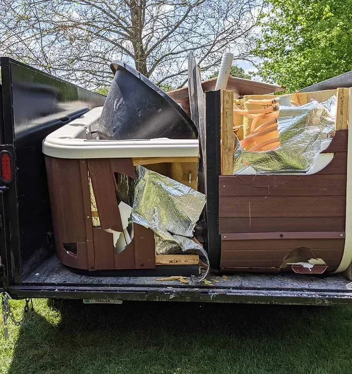 A dismantled brown hot tub inside a black trailer, with foam insulation and reflective foil exposed.