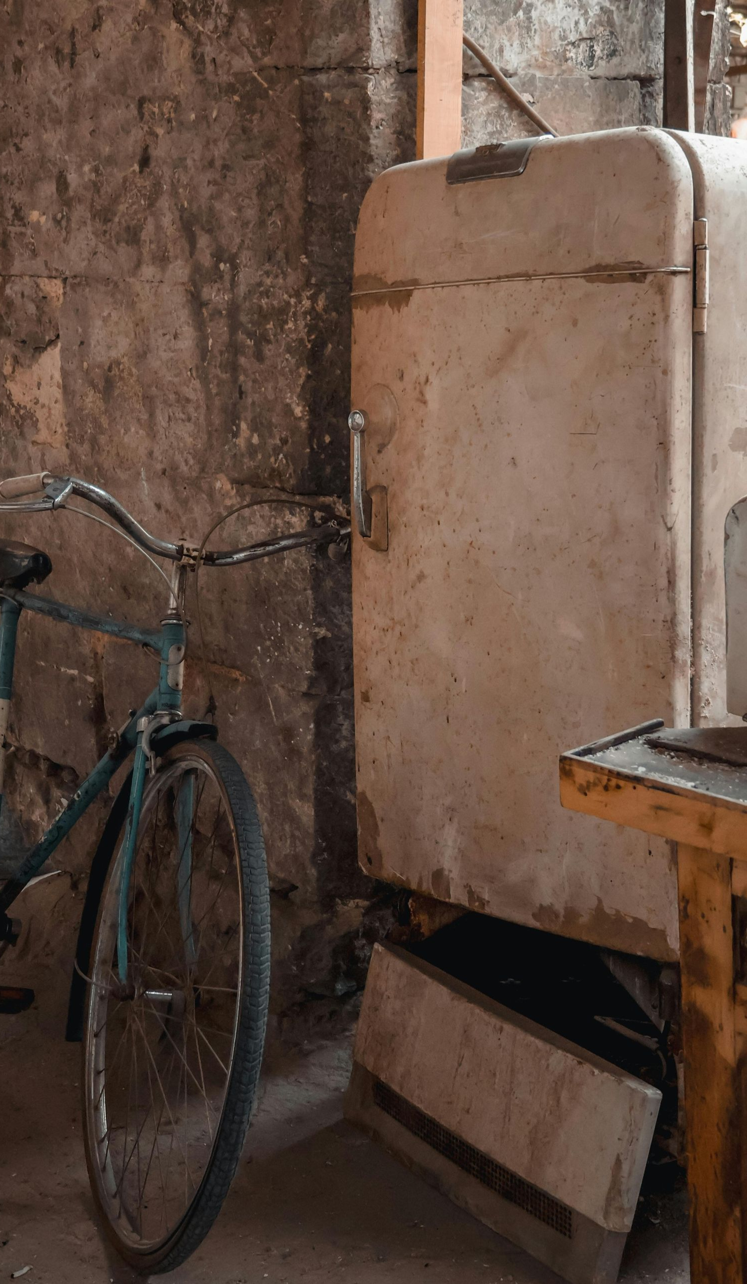 Old, dirty refrigerator and bicycle in a weathered room.