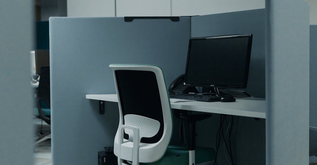 Office cubicle with a computer and white chair. Desk is clear. Grey walls.