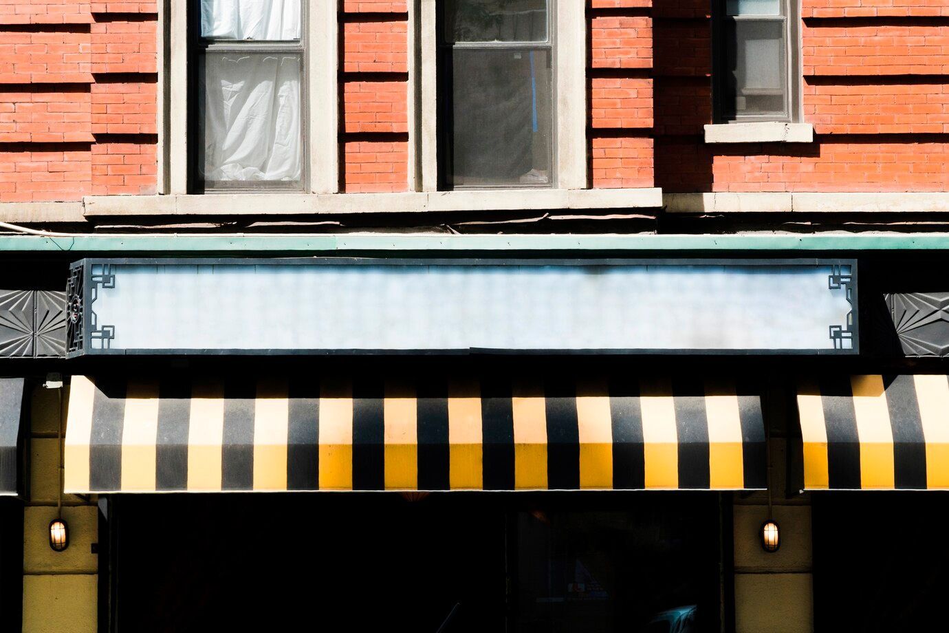 Exterior of a brick building with a blank sign, striped awning, and windows.